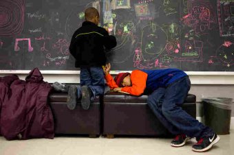 Nikia Cliff II, 6, colors on the chalkboard inside the Major Chords for Minors office before his piano lesson, while his older brother Khalil Cliff, 10, takes a nap before his drum lesson.